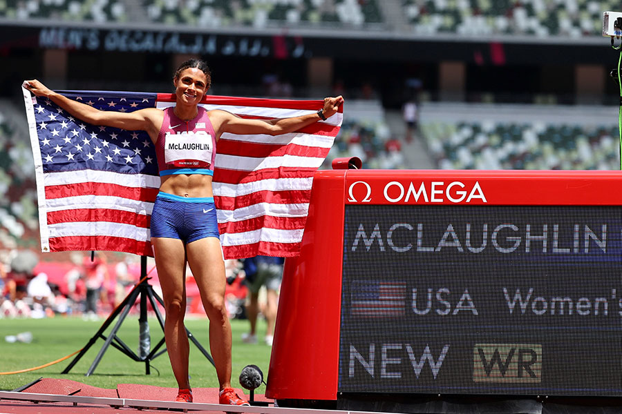 McLaughlin stands with american flag infront of teleprompter and crowd